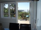 Utsikt från allrummet och matplatsen genom helglasad verandadörr. Till vänster finns bäddsoffa med plats för 2 personer i dubbelsäng.